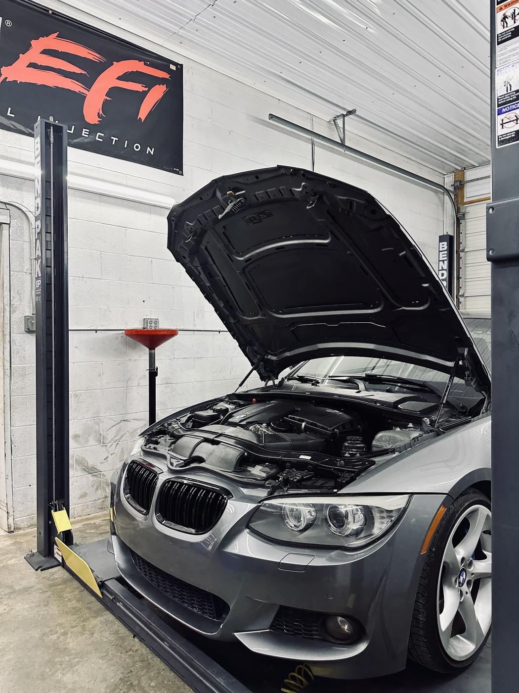 A gray coupe on the lift with its hood raised in a clean bay